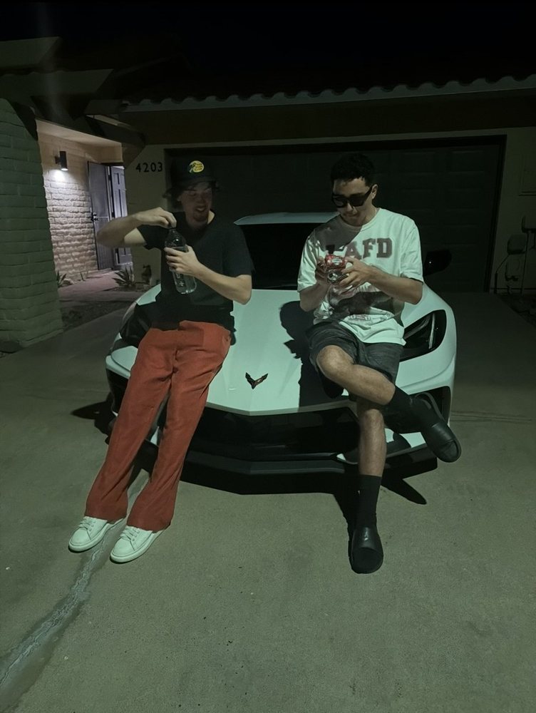 Evan and a friend sitting on a white Corvette at night
